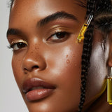 Close-up of a woman with braided hair and serum dropper earrings against a neutral background