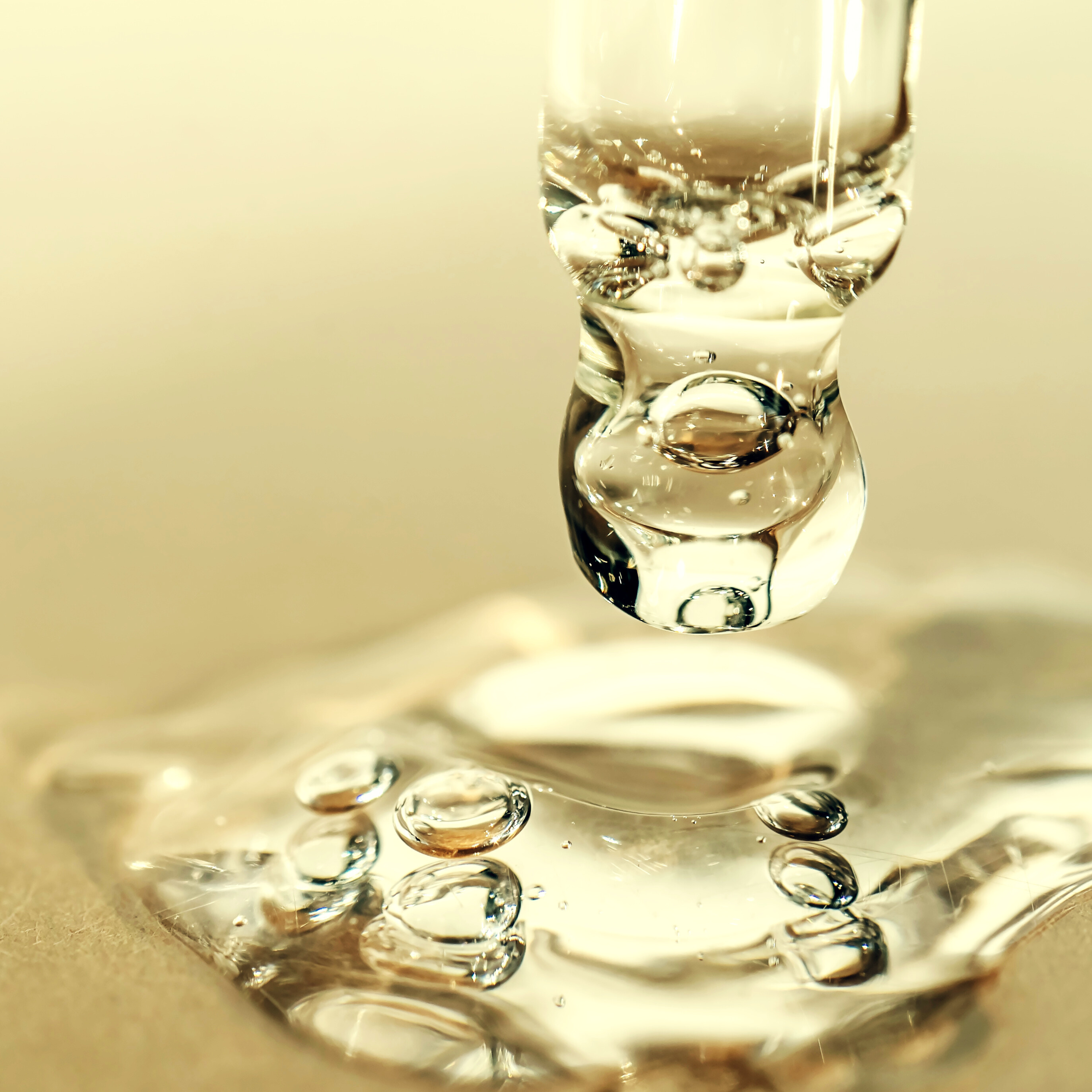 Close-up of a glass eye dropper dispensing Vitamin E oil, a key ingredient in Radiant Shield antioxidant oil on a reflective surface